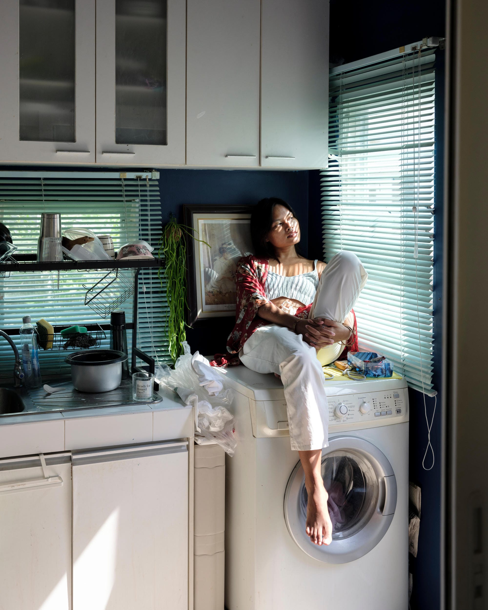 Sacha Piisasha seated on a washing machine beside a kitchen counter at home in Nonthaburi.