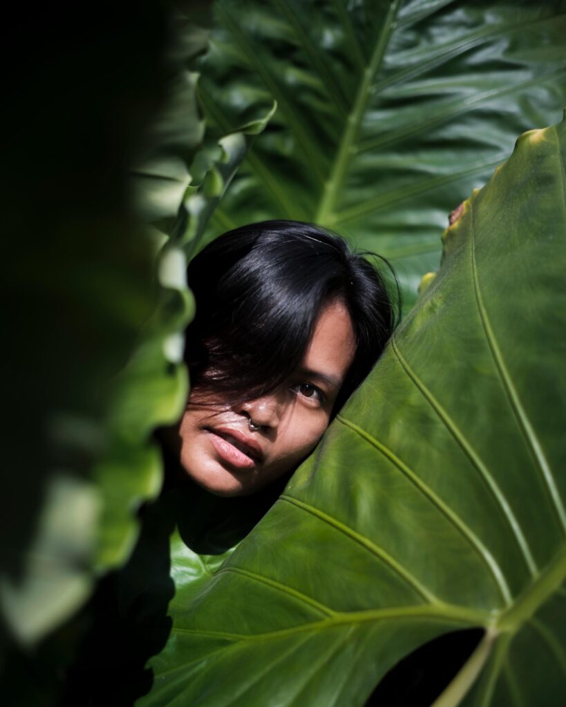 Sacha Piisasha's face framed by large green leaves in Nonthaburi.