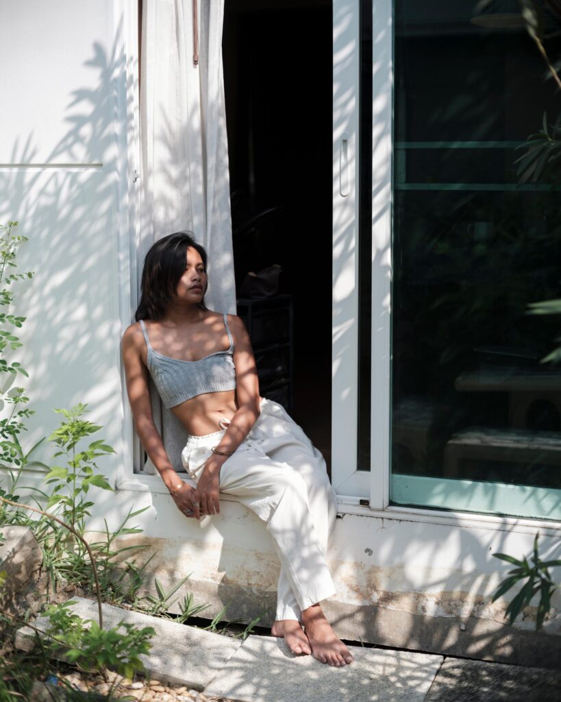 Sacha Piisasha seated outside a window with leafy shadows across the wall in Nonthaburi.