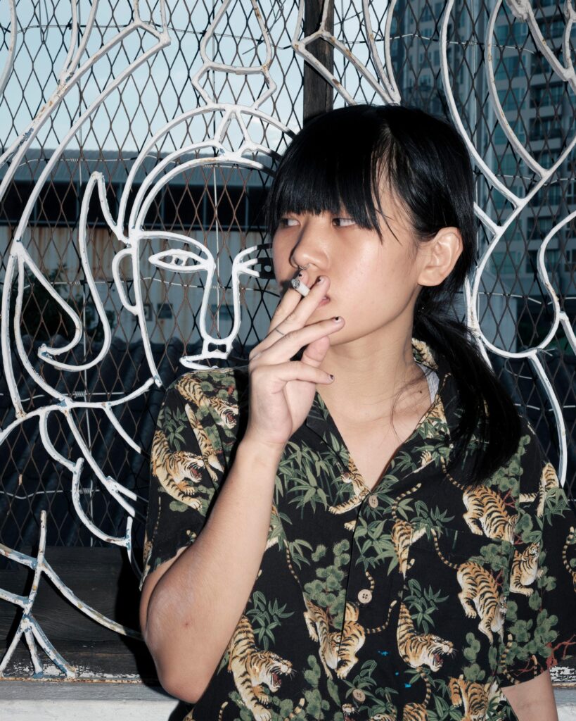 Sandee smoking beside a window covered with white line drawings in Bangkok.