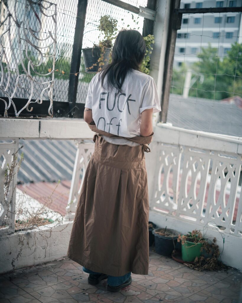 Sandee standing on a Bangkok balcony with writing on the back of her white shirt.