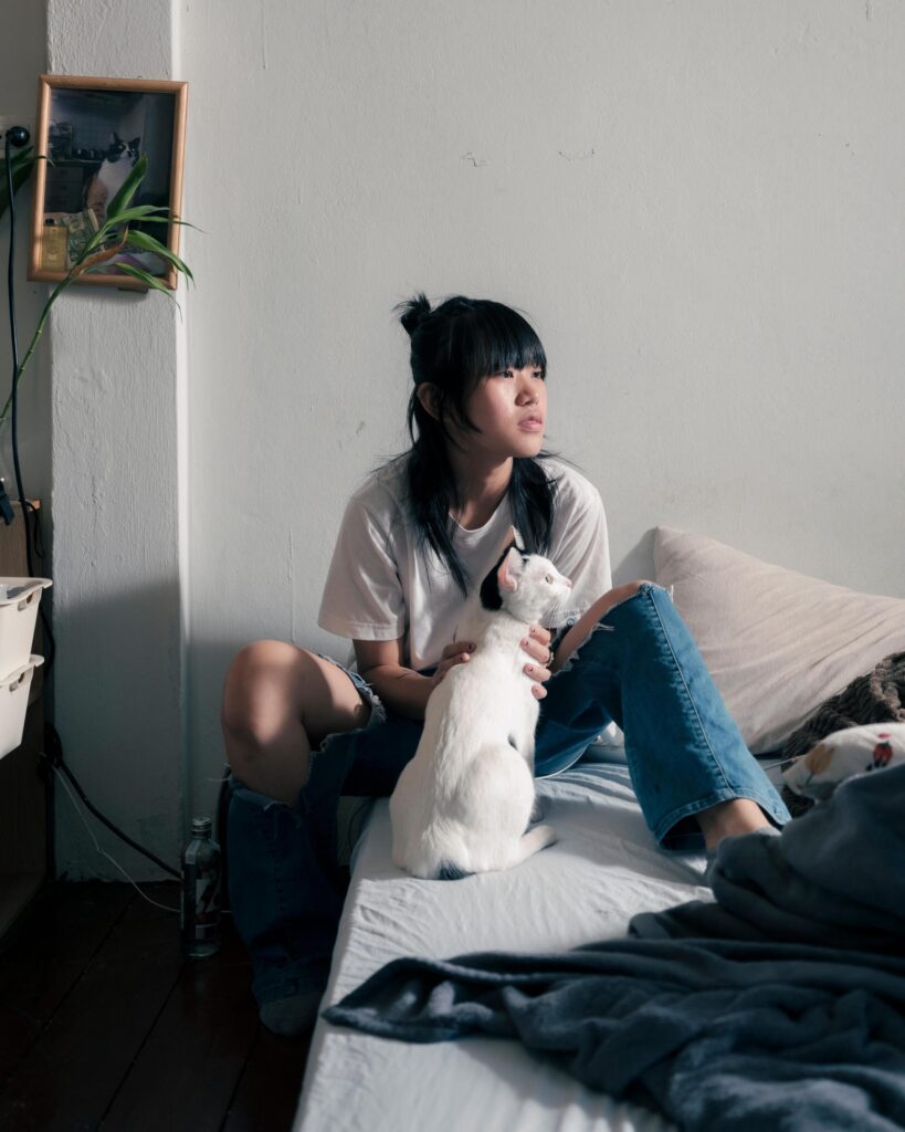 Sandee sitting on a bed with a white cat at home in Bangkok.